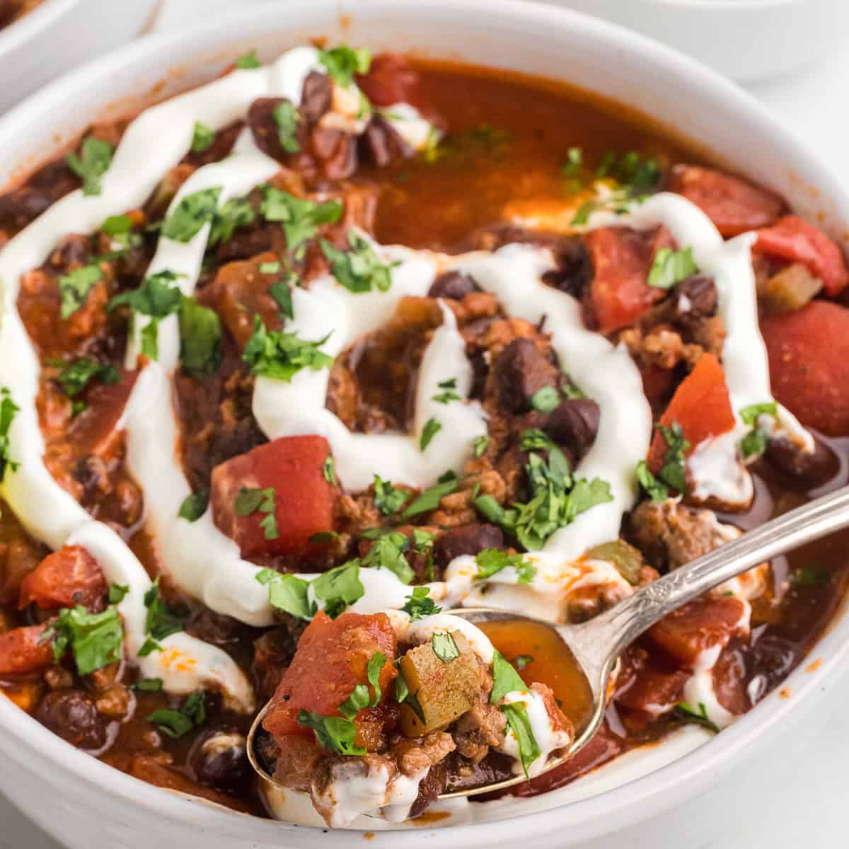 Finished chili in a white serving bowl with a garnish of sour cream and cilantro.