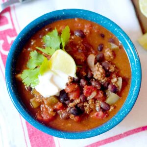 A bowl of black bean chili with sour cream, cilantro, and a lime wedge on top.