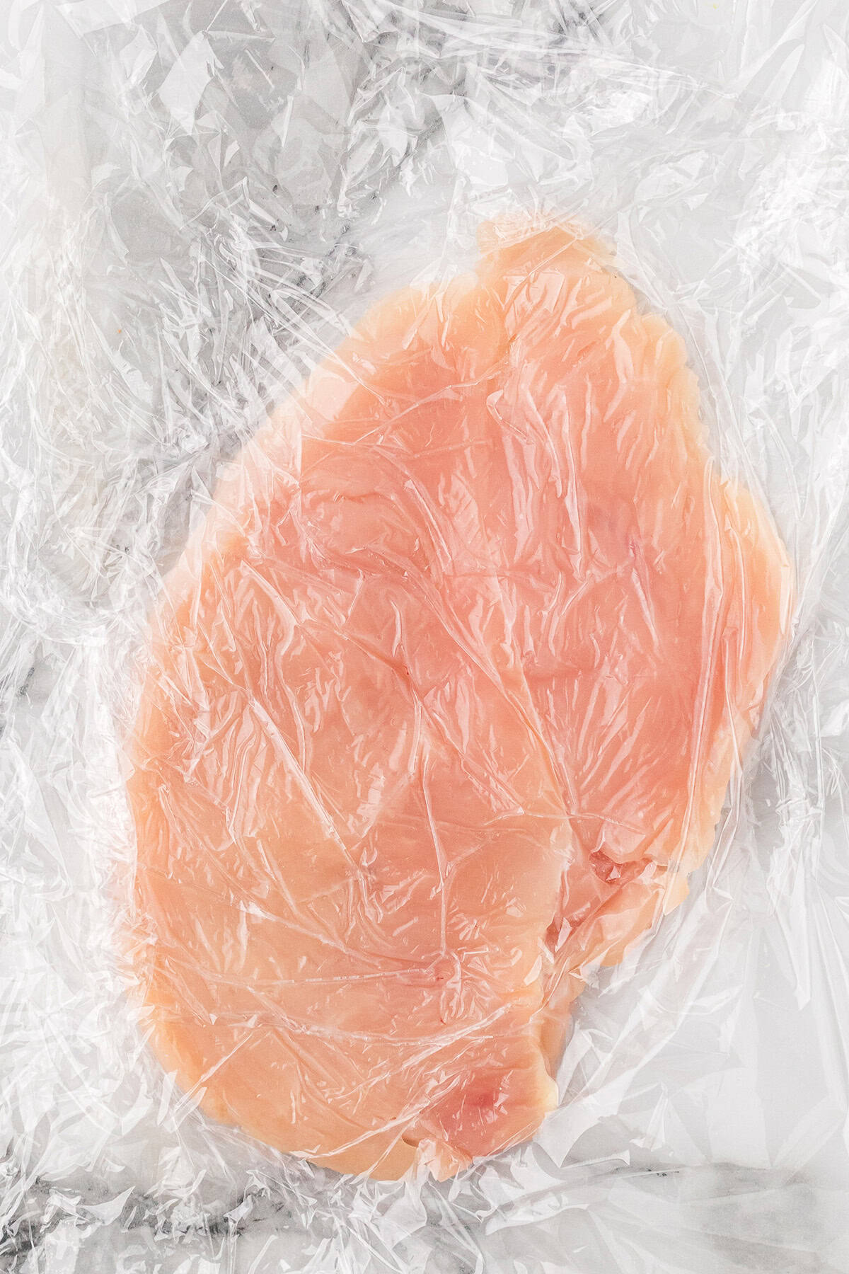 Chicken breast pounded between plastic wrap.