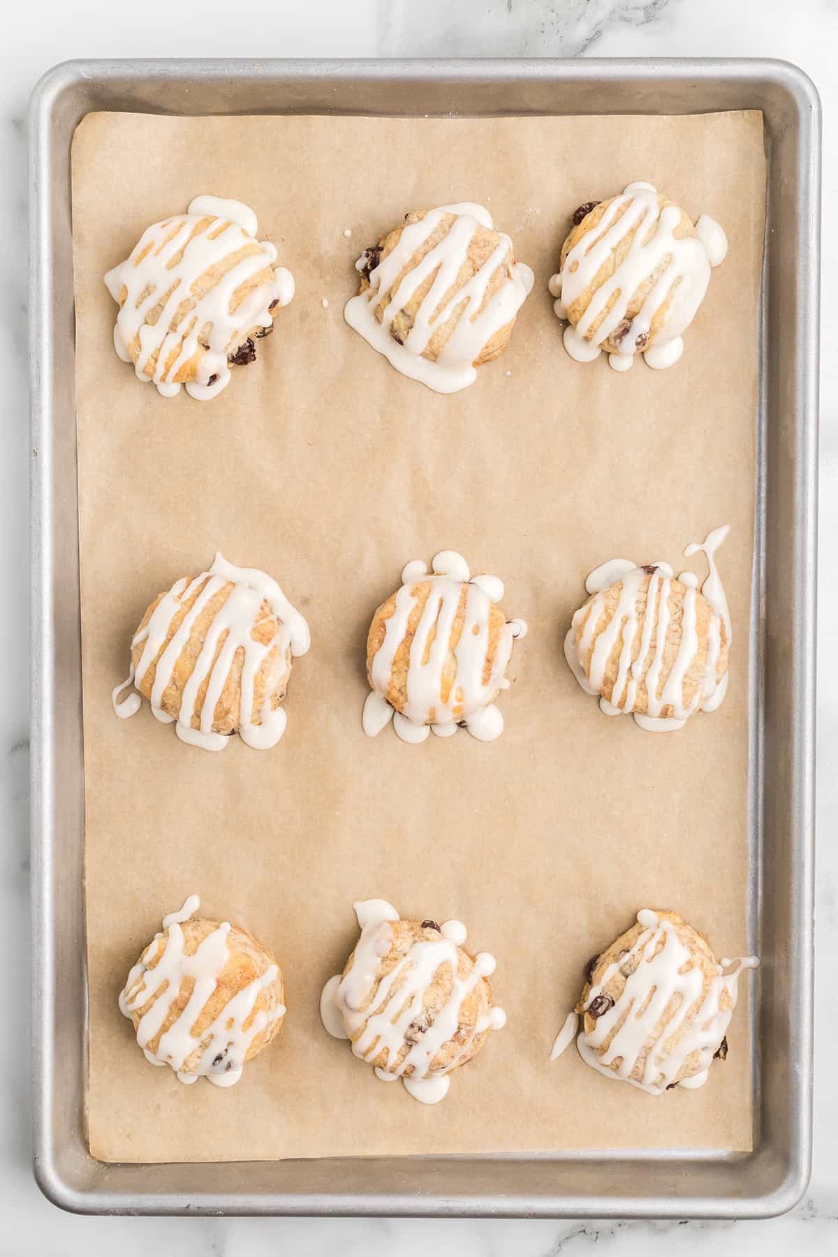Nine iced biscuits arranged on a parchment-lined baking sheet, viewed from above.
