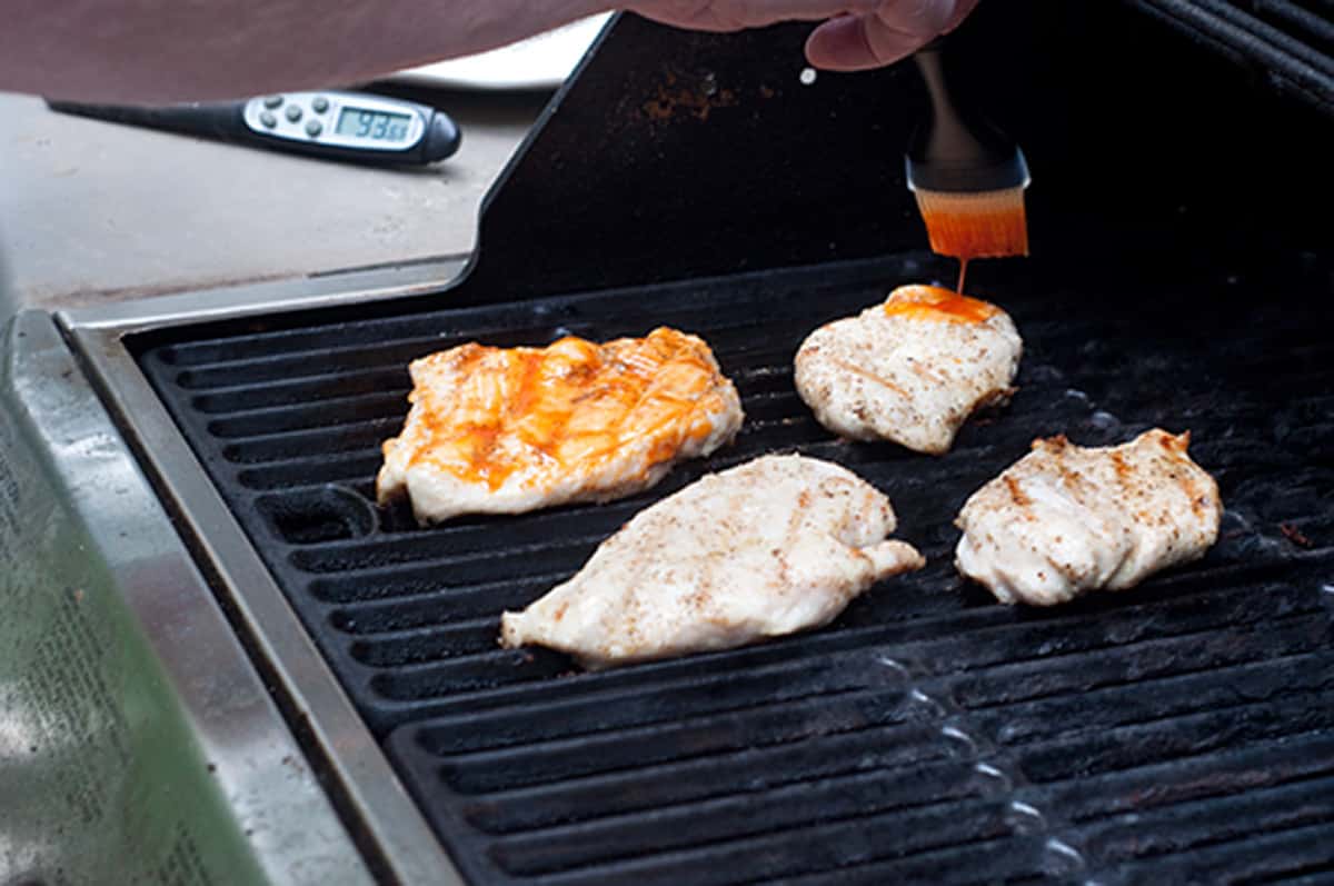 Chicken breasts brushed with buffalo wing sauce cooking on a grill.