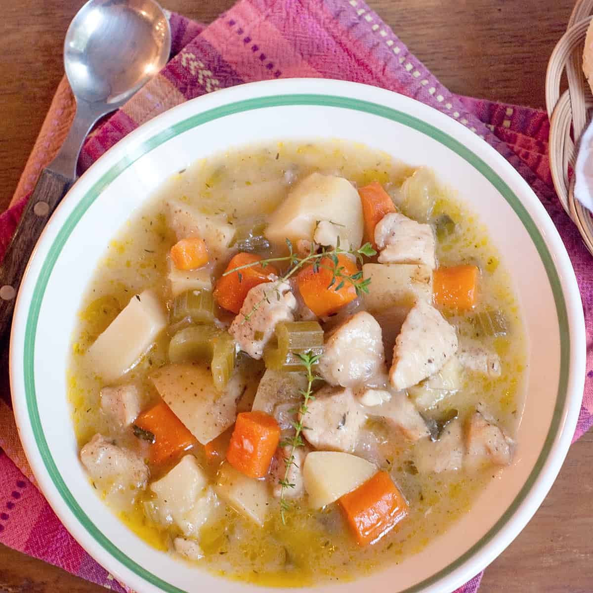 A bowl of chicken stew with a basket of biscuits on the side.