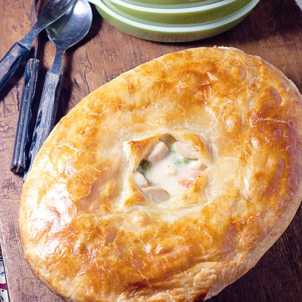 Classic chicken pot pie in a serving dish on a wooden board.