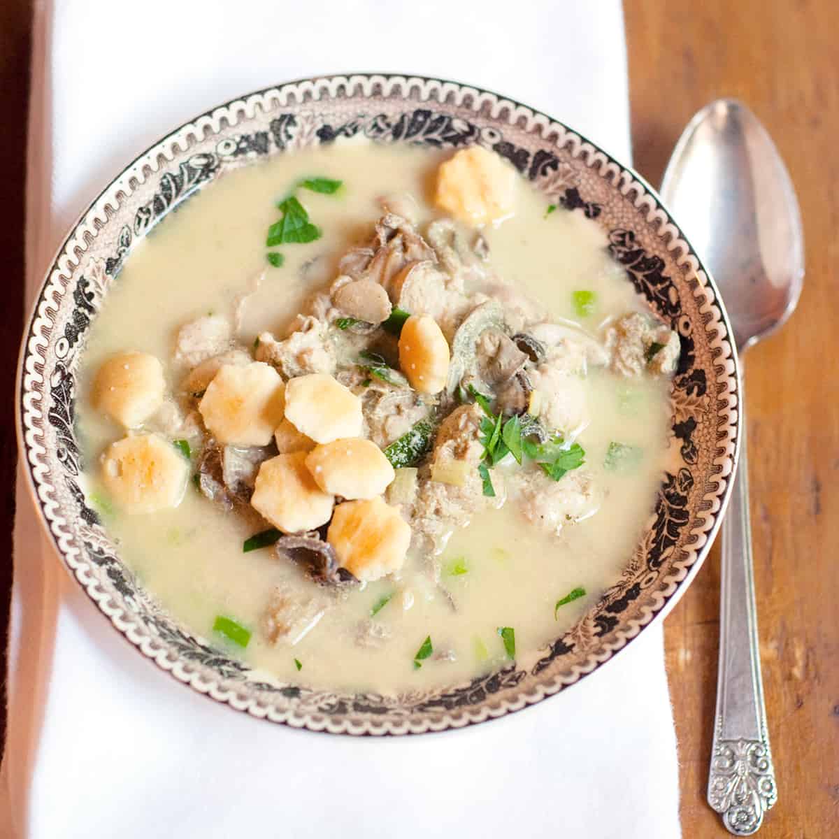 A serving of oyster stew in a bowl with a napkin and spoon alongside.