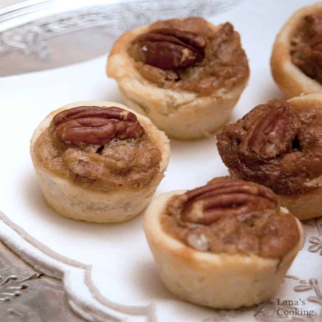 Mini pecan tarts arranged on a white napkin atop a silver tray.