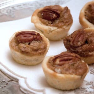 Mini pecan tarts arranged on a white napkin atop a silver tray.