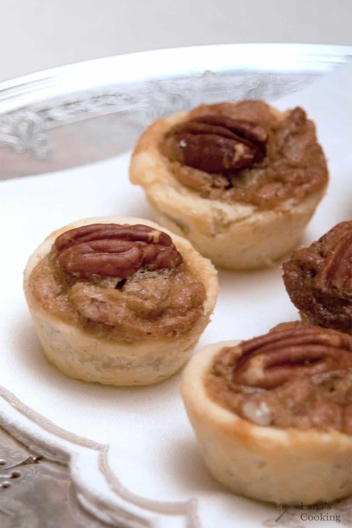 Three mini pecan tarts on a white napkin, served on a silver tray.