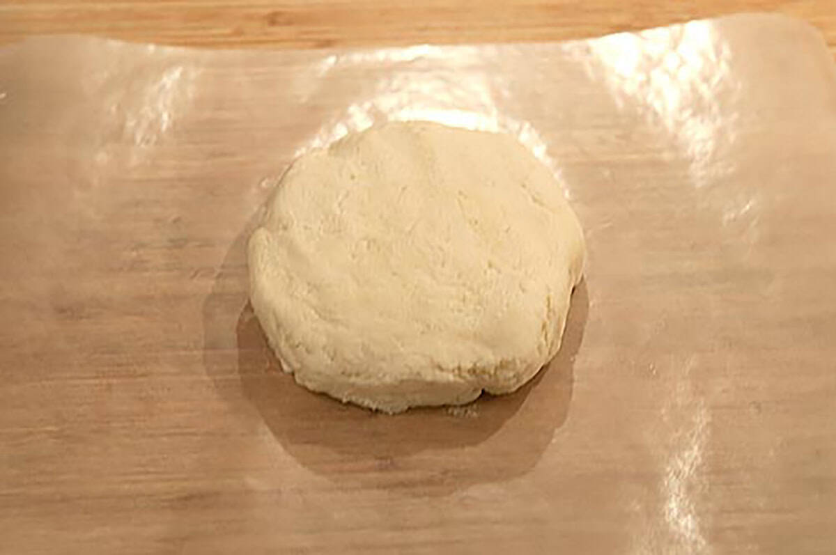 A round disk of dough sits on a sheet of wax paper on a wooden surface.