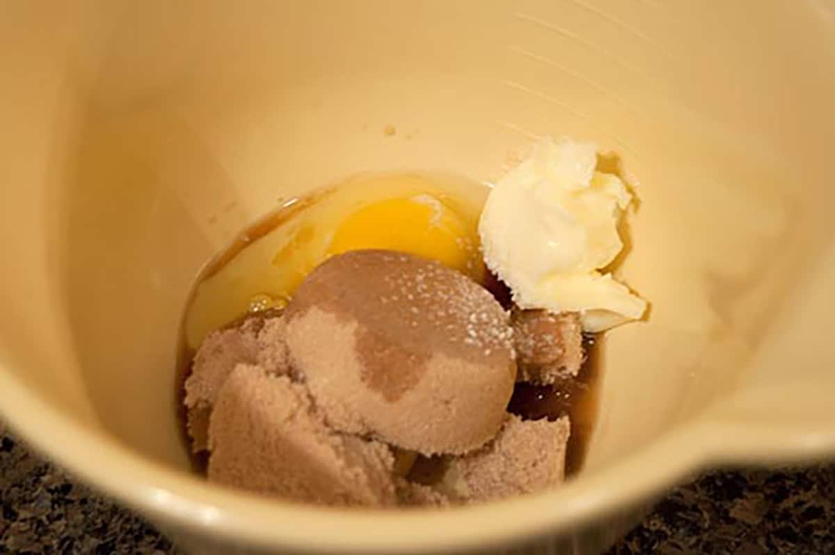 A mixing bowl with brown sugar, an egg, butter, and vanilla extract inside.