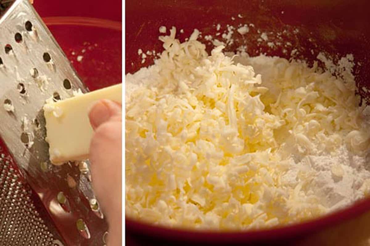 Hand grating cold butter with a box grater beside a bowl of grated butter and flour.