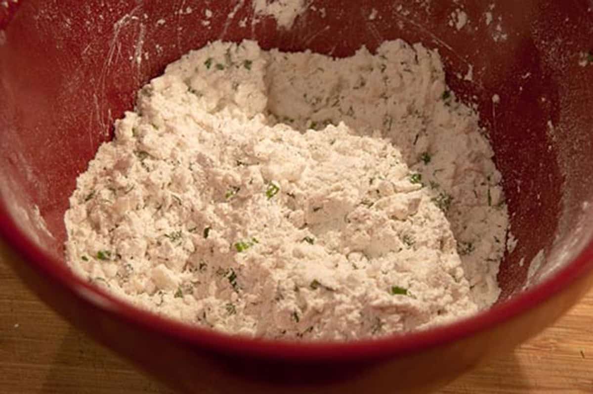 Bowl with flour mixture and chopped herbs, ready to be mixed for baking.