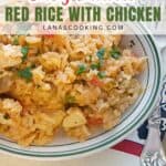 A plate of red rice with chicken, garnished with herbs, beside a fork on a patterned napkin.