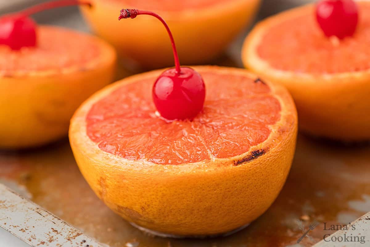 Broiled grapefruit halves topped with maraschino cherries on a baking tray.