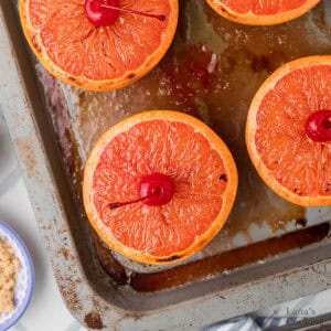 Broiled grapefruit halves topped with maraschino cherries on a baking sheet.