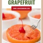 Half a broiled grapefruit in a white bowl, topped with a cherry, with a fork lifting a bite.