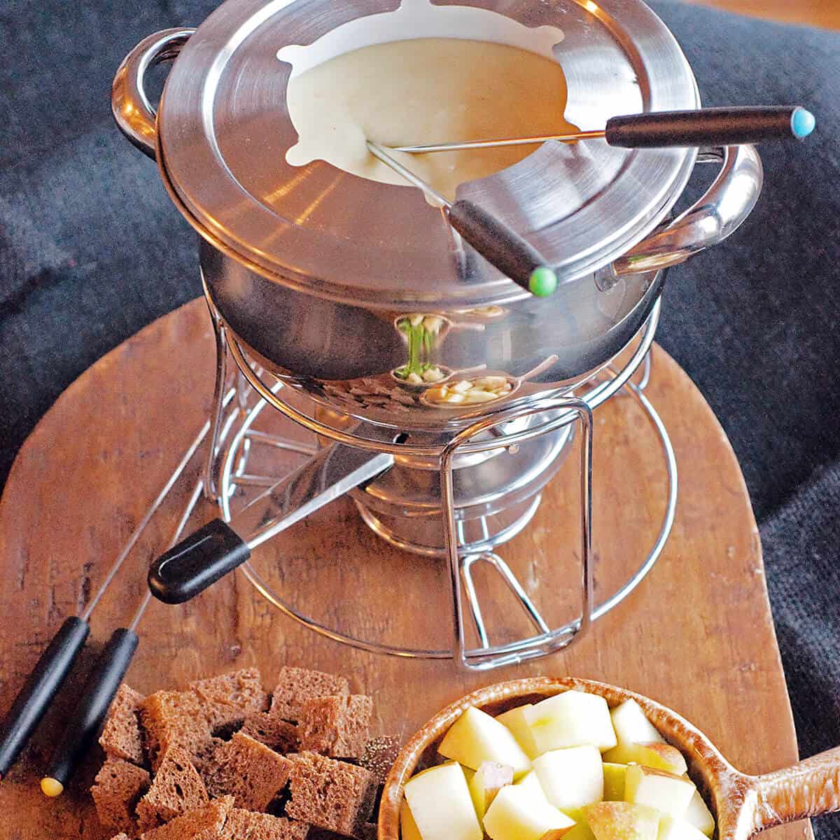 Cheese fondue in pot with bread and vegetable dippers.