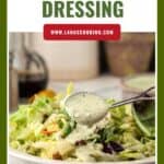 A spoon drizzles green goddess dressing over a fresh salad in a white bowl.