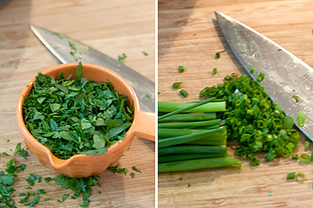 Chopped fresh herbs in an orange measuring cup and sliced green onions on a wooden cutting board, with a knife nearby.