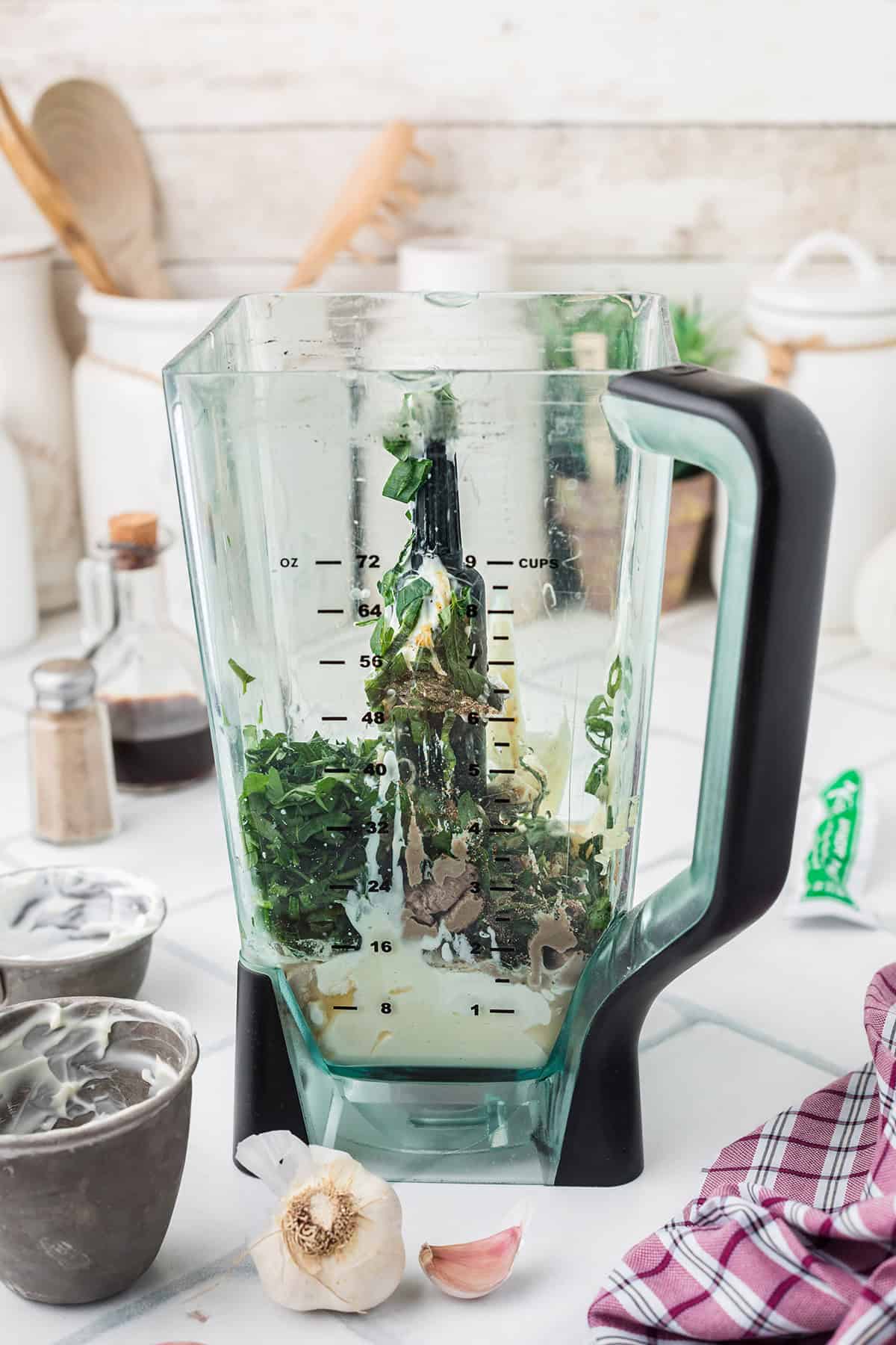 A blender contains chopped green onions, garlic, and other ingredients on a kitchen counter with utensils nearby.