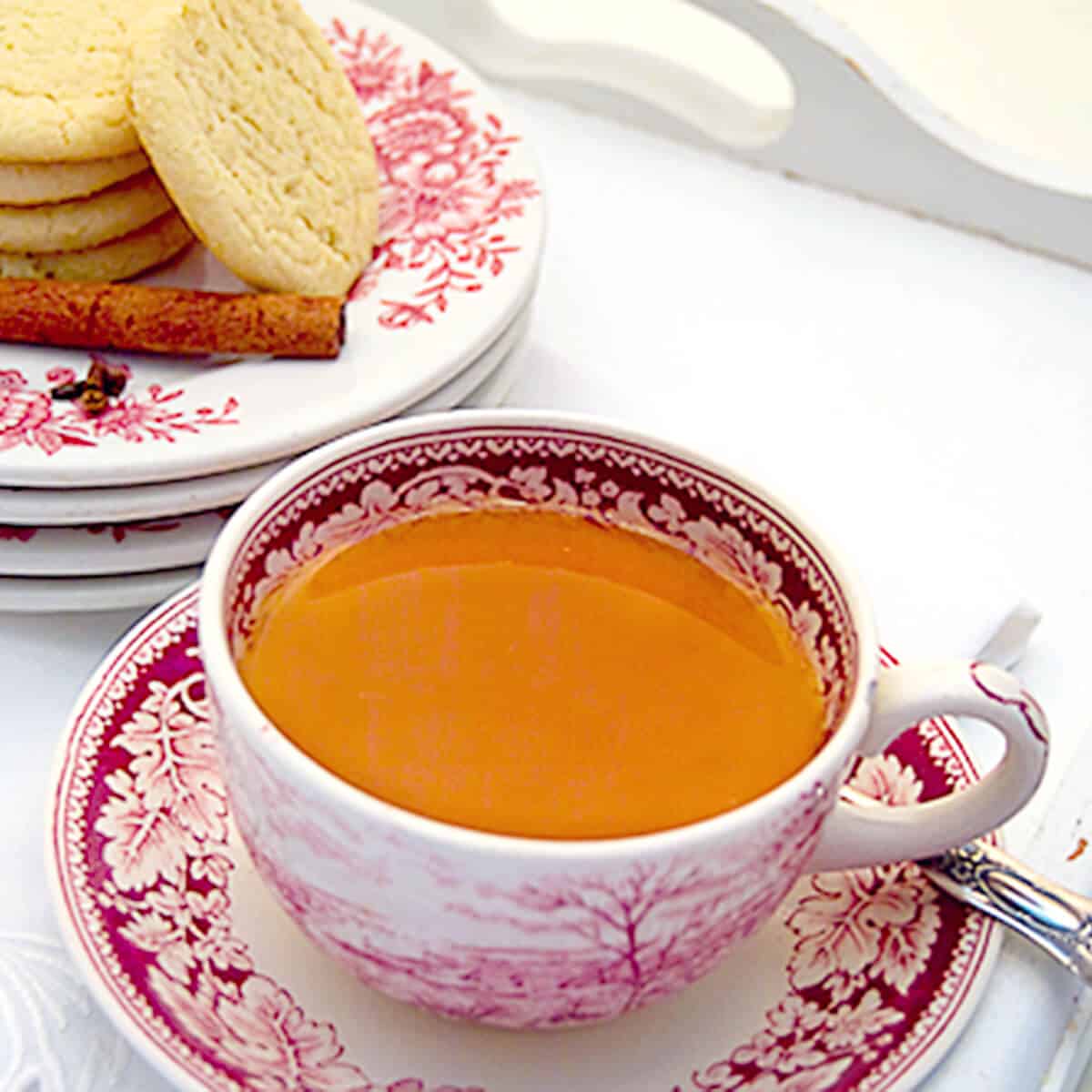 A cup of hot spiced tea with a plate of cookies in the background.