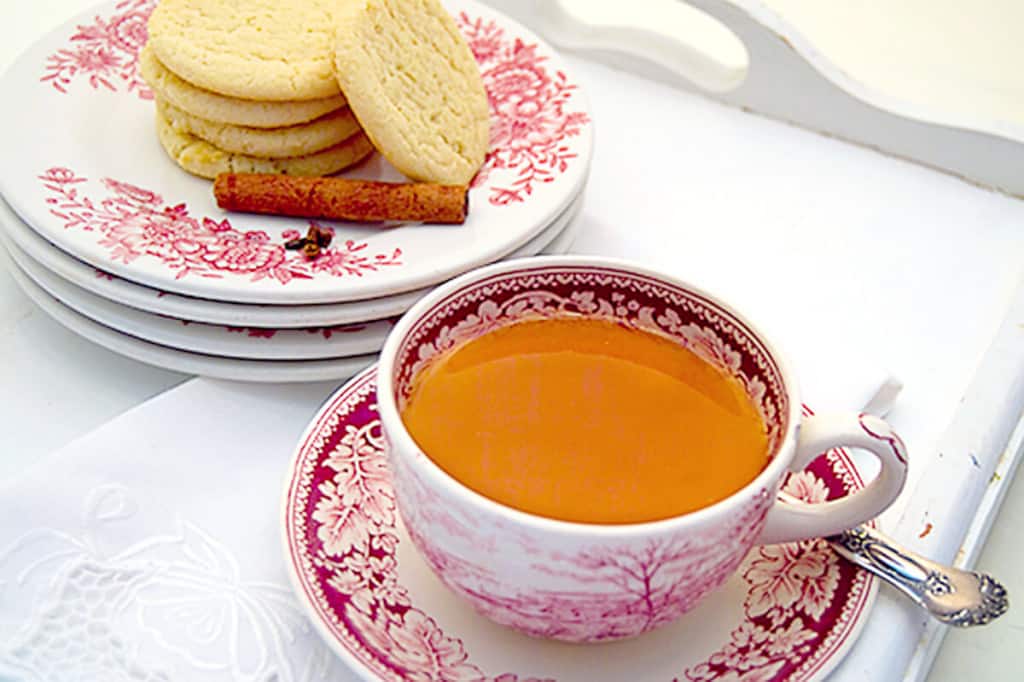 A cup of hot spiced tea with a plate of cookies in the background.