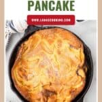 A golden Dutch baby pancake in a cast iron skillet, topped with powdered sugar, on a marble surface.