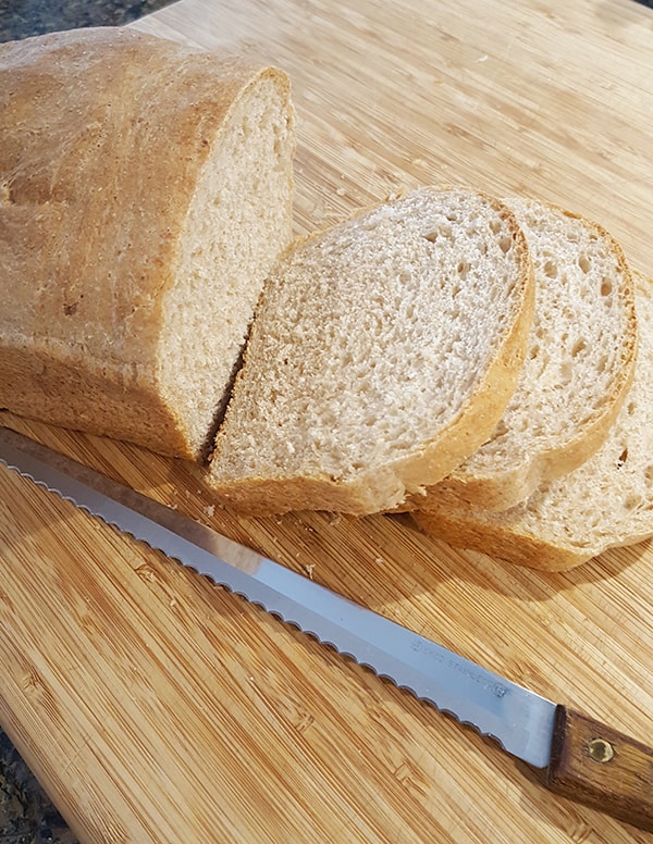 Sliced loaf of bread with a knife on a cutting board.