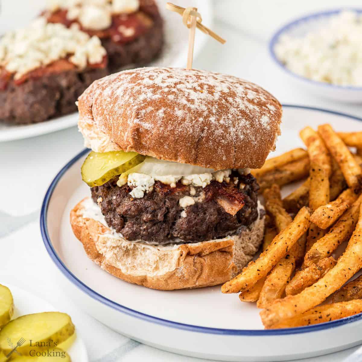 Bacon cheeseburger with blue cheese on a white plate with french fries.
