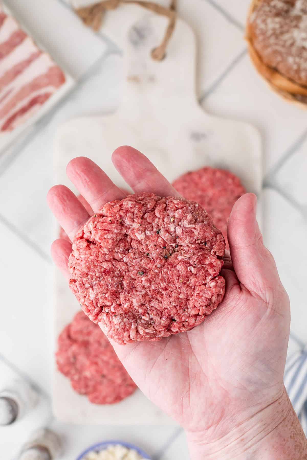 One patty of seasoned ground beef being held on an open hand.