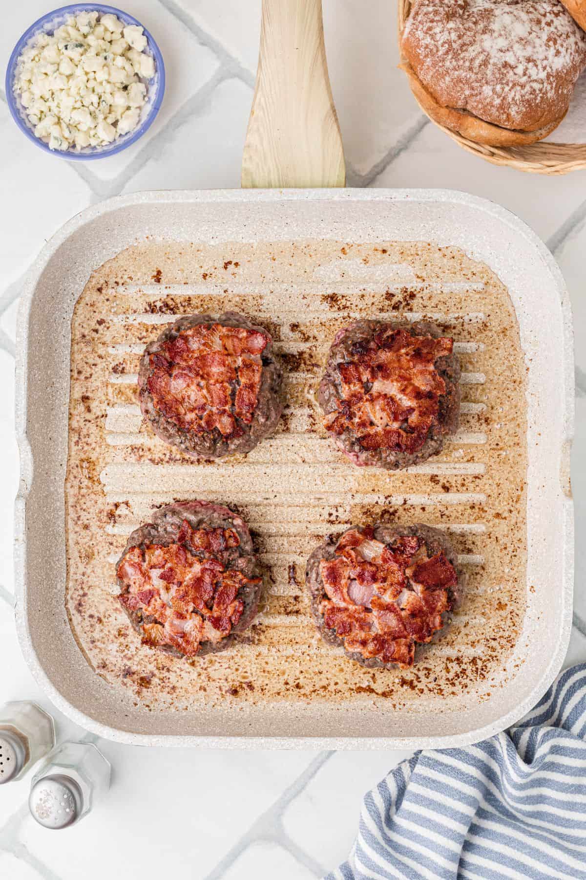 Burger patties after being flipped exposing the cooked bacon.