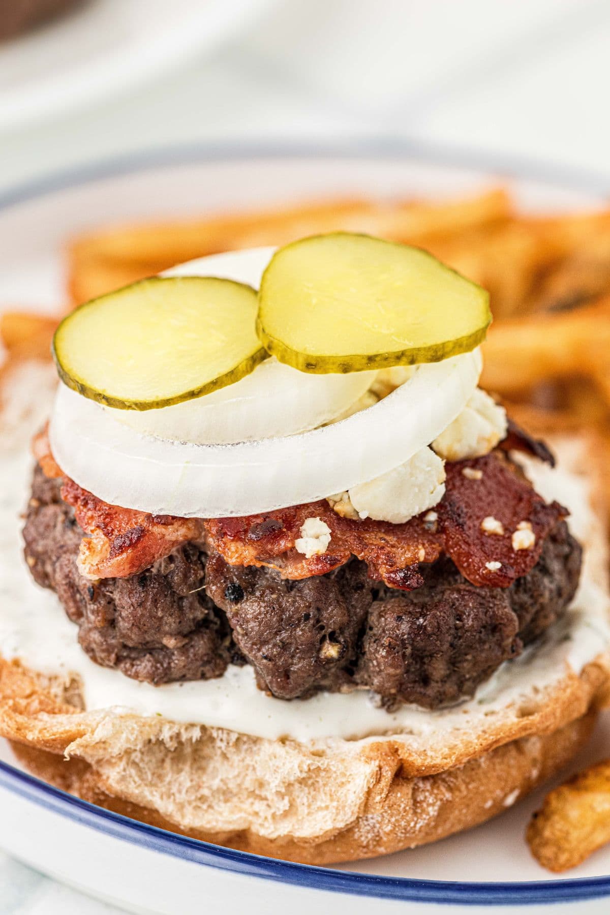 A bacon cheeseburger topped with blue cheese, onion, and slices of pickles.