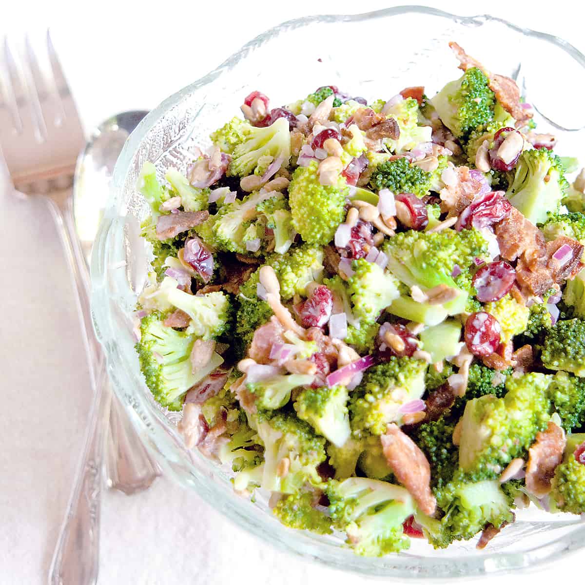 Broccoli Salad in a glass serving bowl with vintage serving utensils.