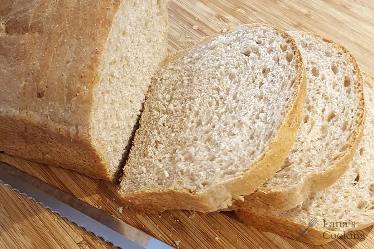 Loaf of sliced bread on a wooden cutting board with a serrated knife.