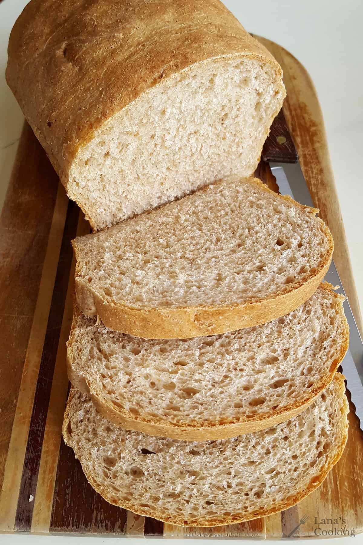 A loaf of sliced bread on a wooden cutting board with a serrated knife.