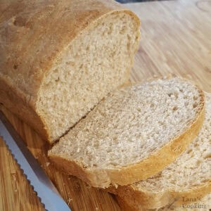 A loaf of sliced bread and a serrated knife on a wooden cutting board.