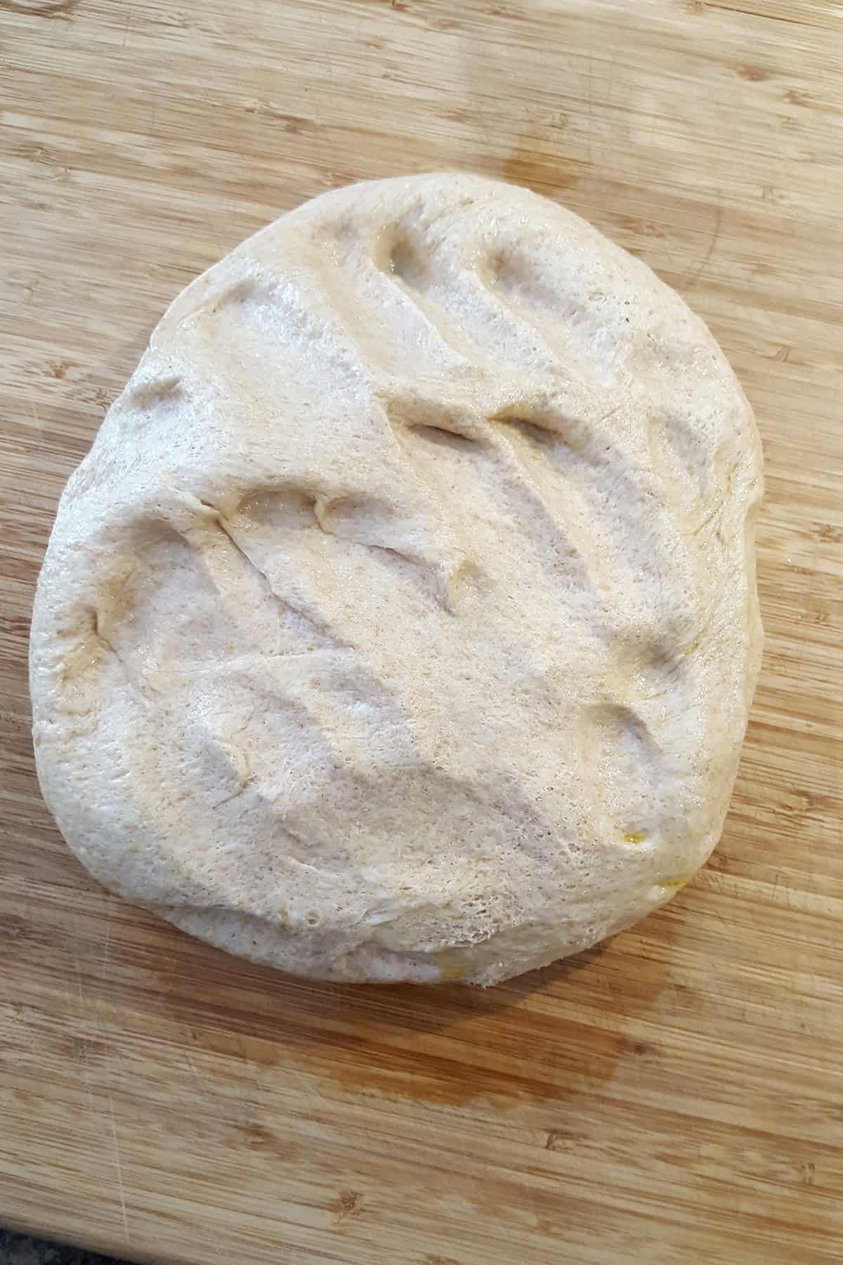A ball of raw bread dough on a wooden cutting board.