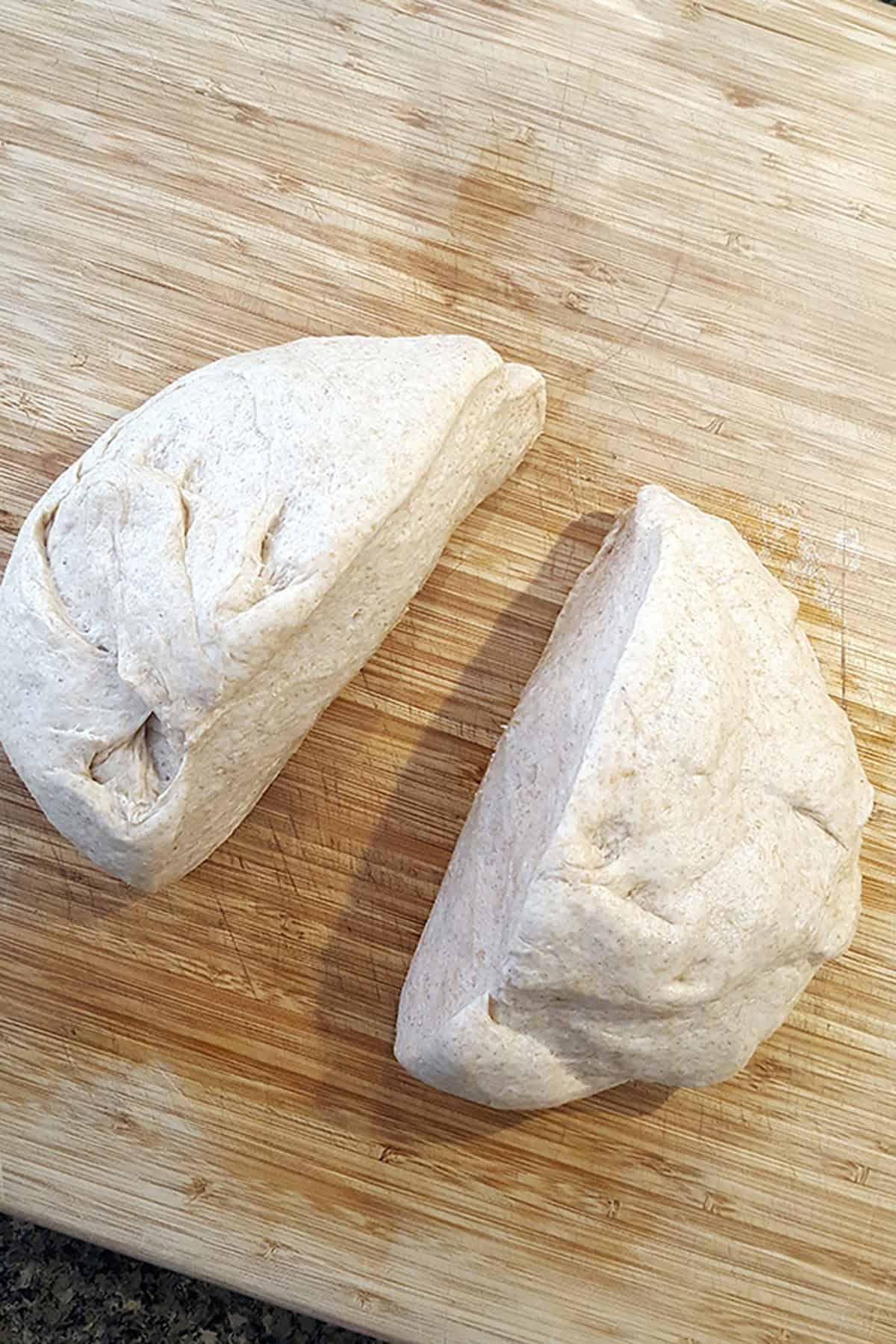 Two mounds of raw bread dough on a wooden cutting board.