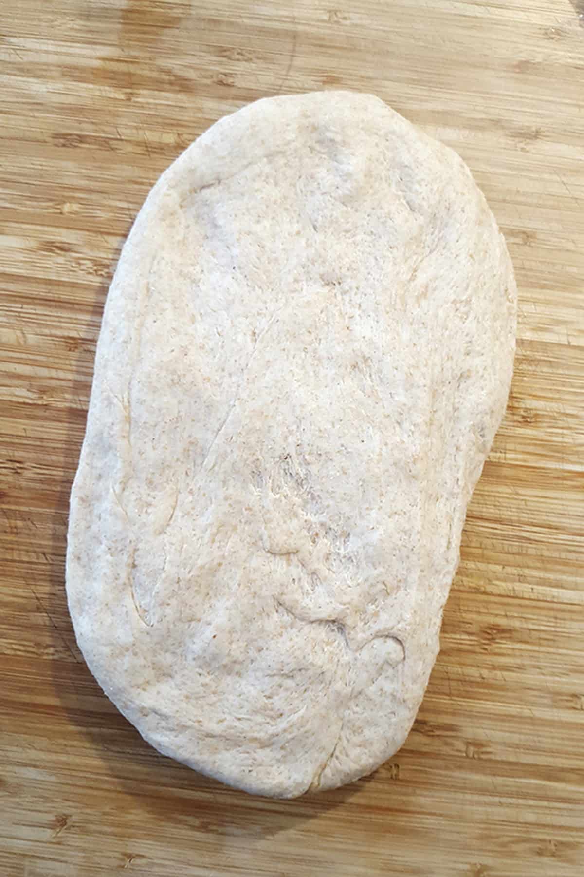 A round of unbaked bread dough on a wooden cutting board.