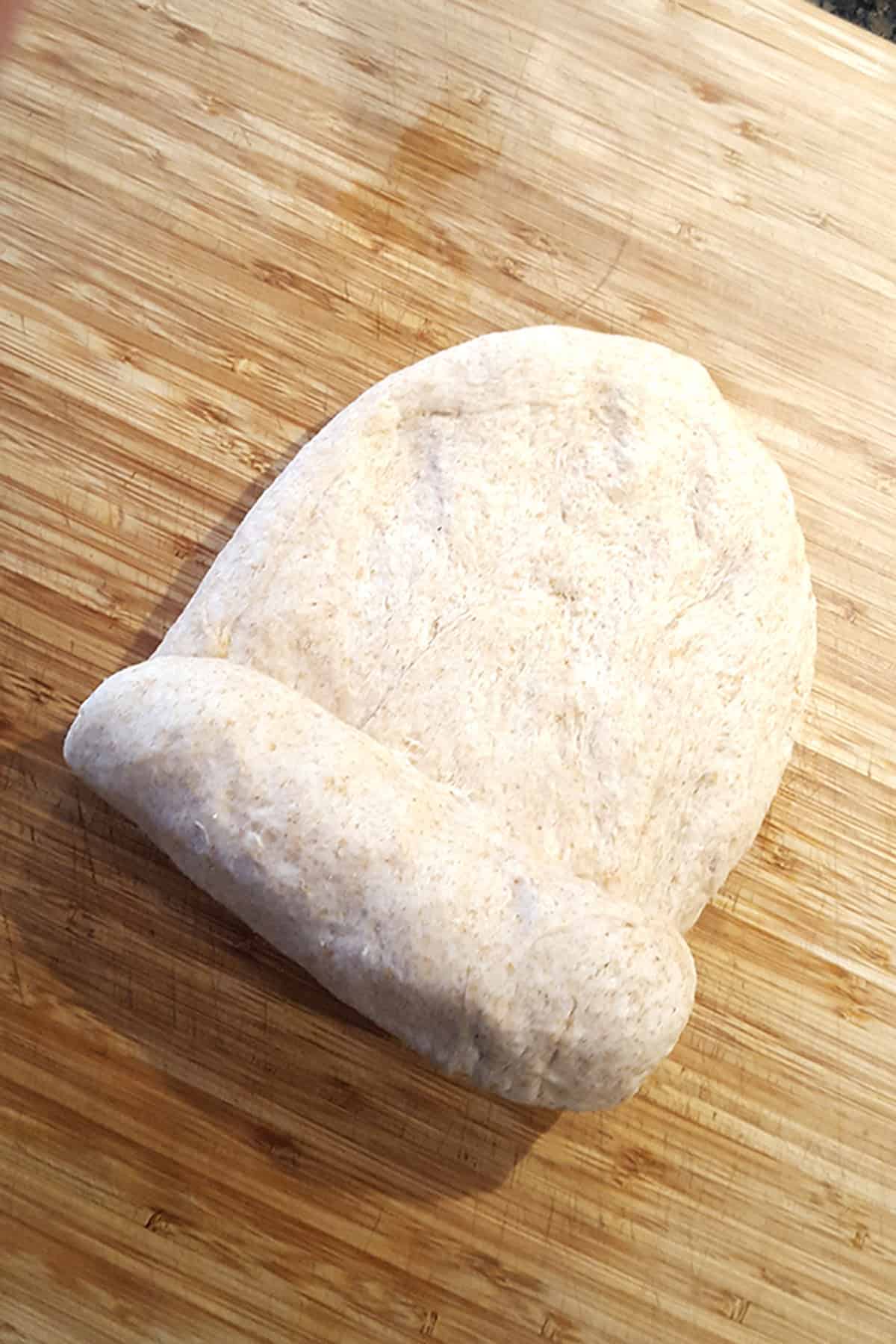 A ball of dough partially rolled up on a wooden cutting board.