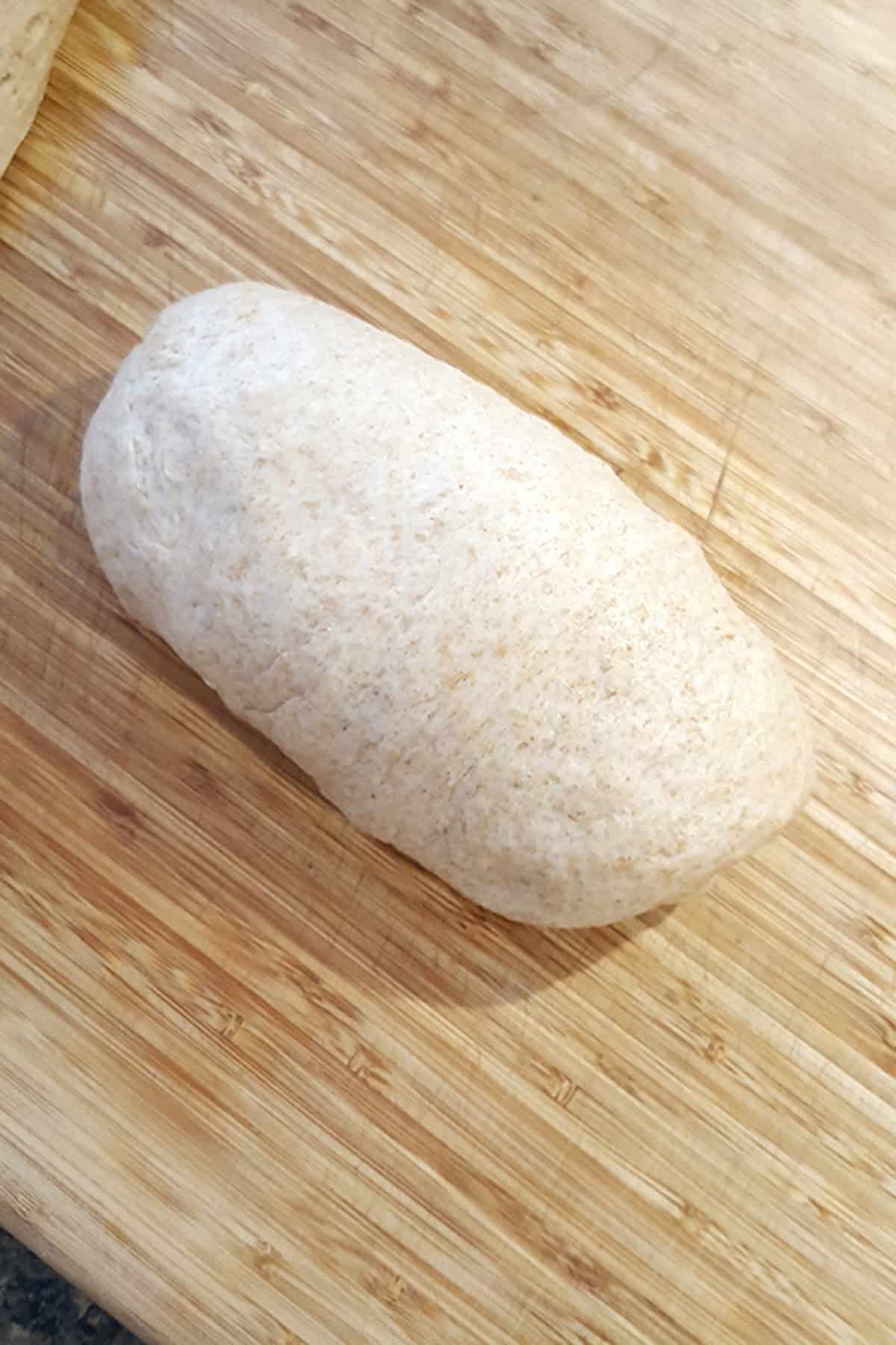 A loaf of raw, unbaked dough on a wooden cutting board.