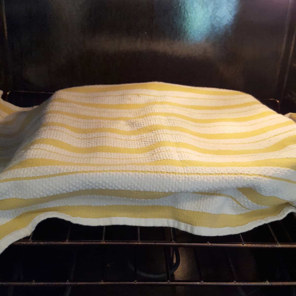 A yellow and white striped kitchen towel covering loaf pans inside an oven.