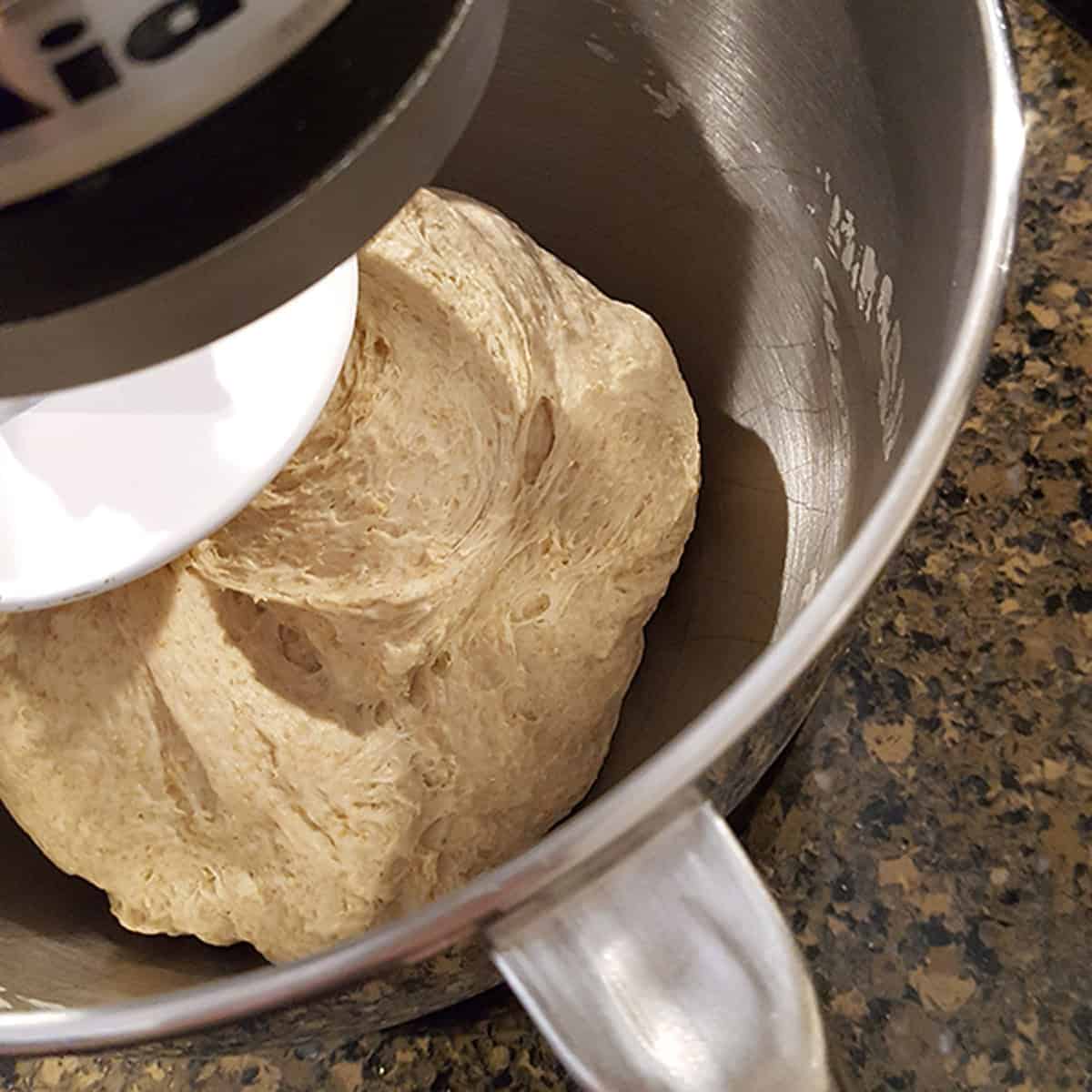 Dough being kneaded in a stand mixer bowl.