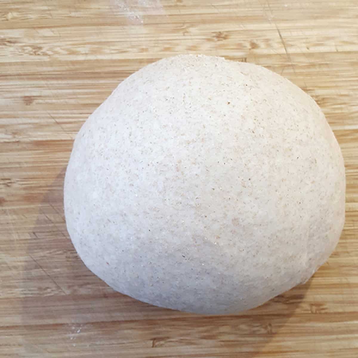 A ball of homemade bread dough on a wooden cutting board.