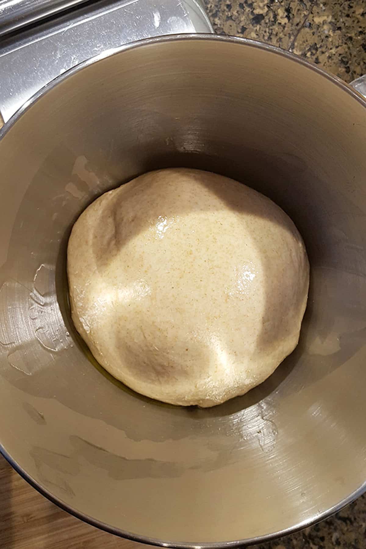 A ball of dough resting in a metal mixing bowl.