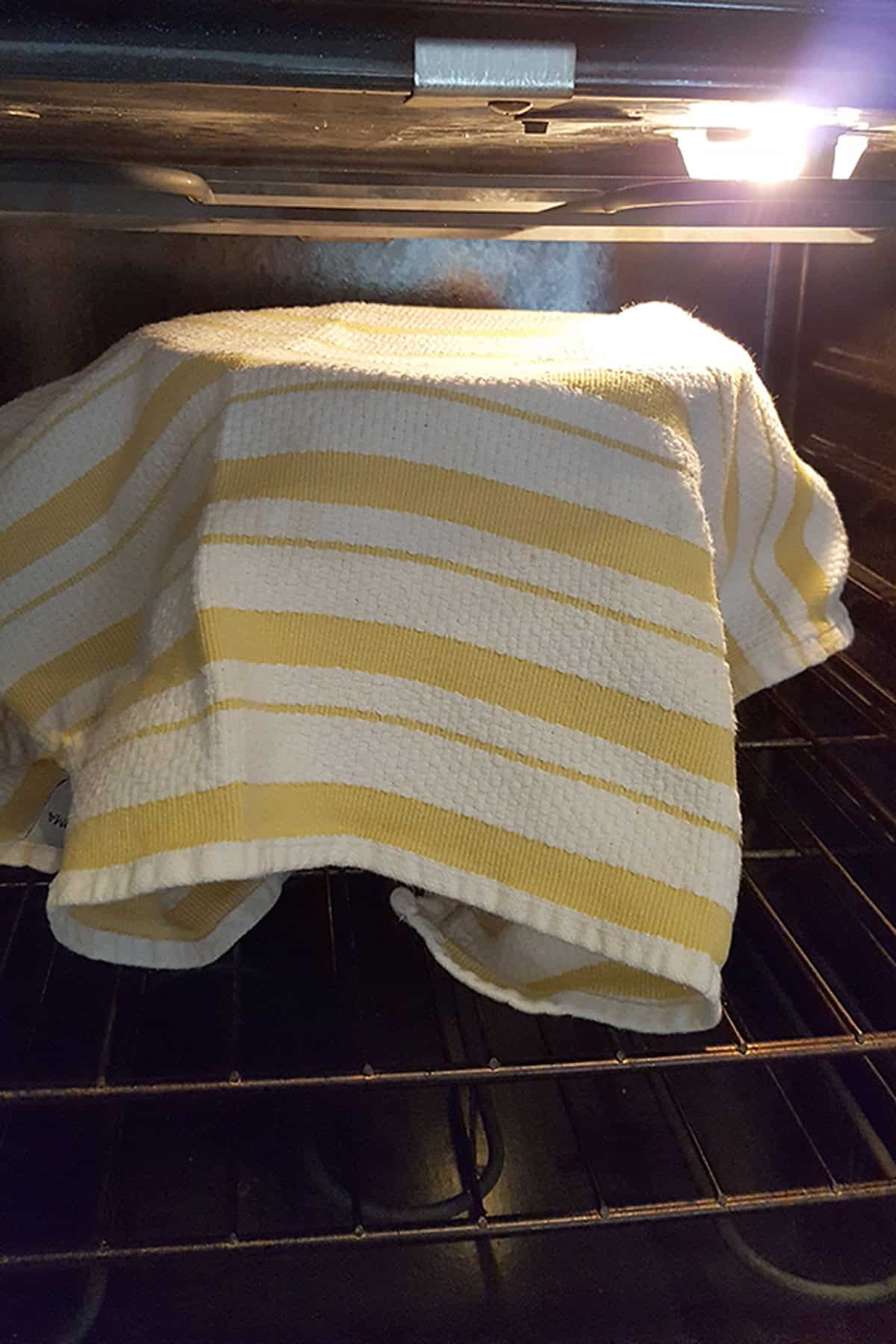 A yellow and white striped kitchen towel covering a bowl inside an oven.