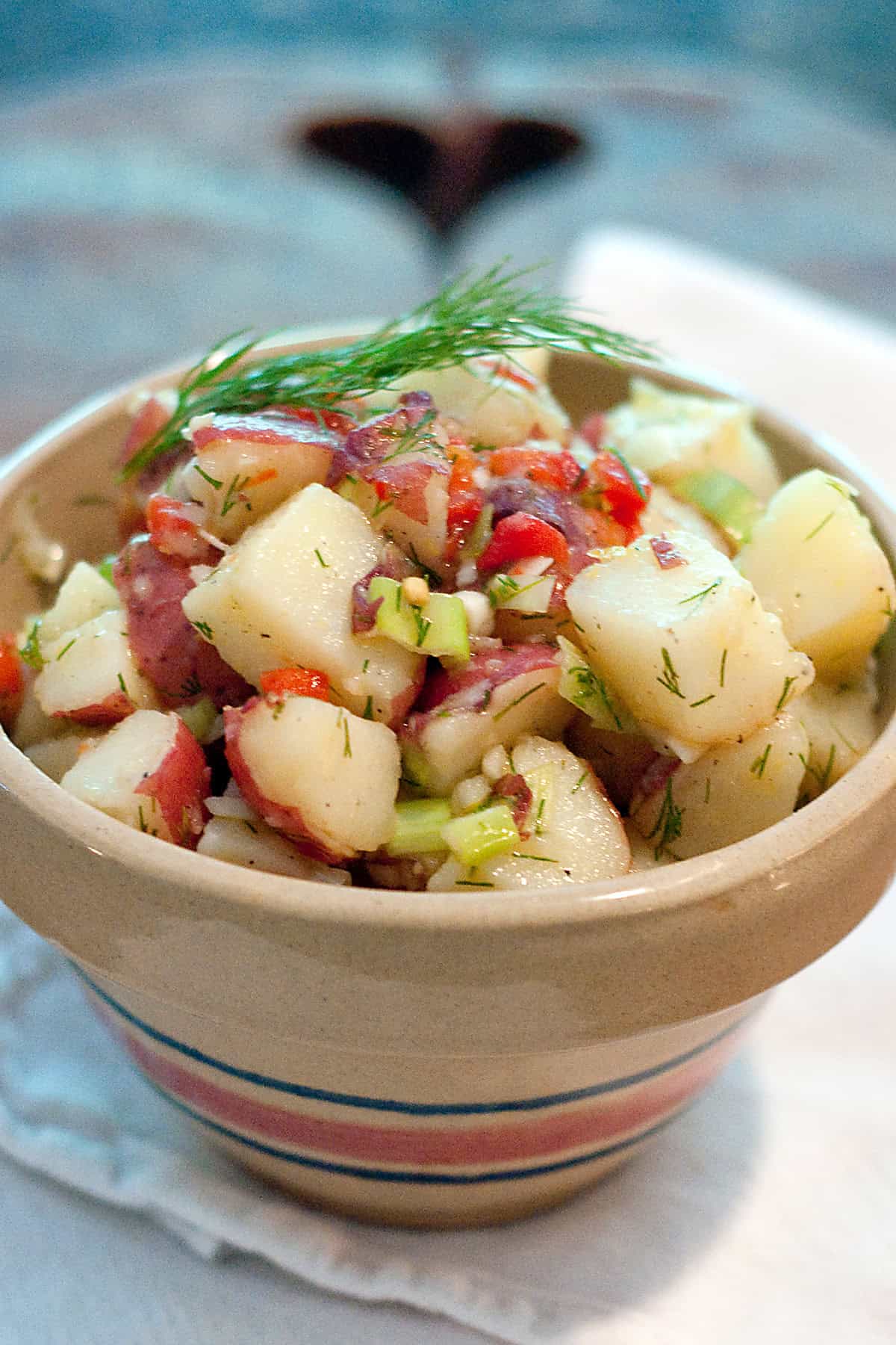 A bowl of potato salad with red potatoes, celery, pimientos, and fresh dill, garnished with a sprig of dill.
