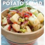 Bowl of lemon dill potato salad with herbs, red potatoes, and pimientos, garnished with fresh dill.