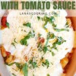 Baked potato gnocchi topped with tomato sauce, melted cheese, grated parmesan, and fresh chopped basil in a beige oval dish.