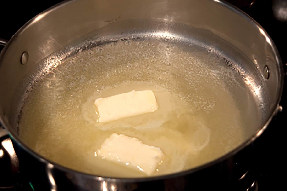Butter and olive oil melting in a stainless steel skillet on a stovetop.