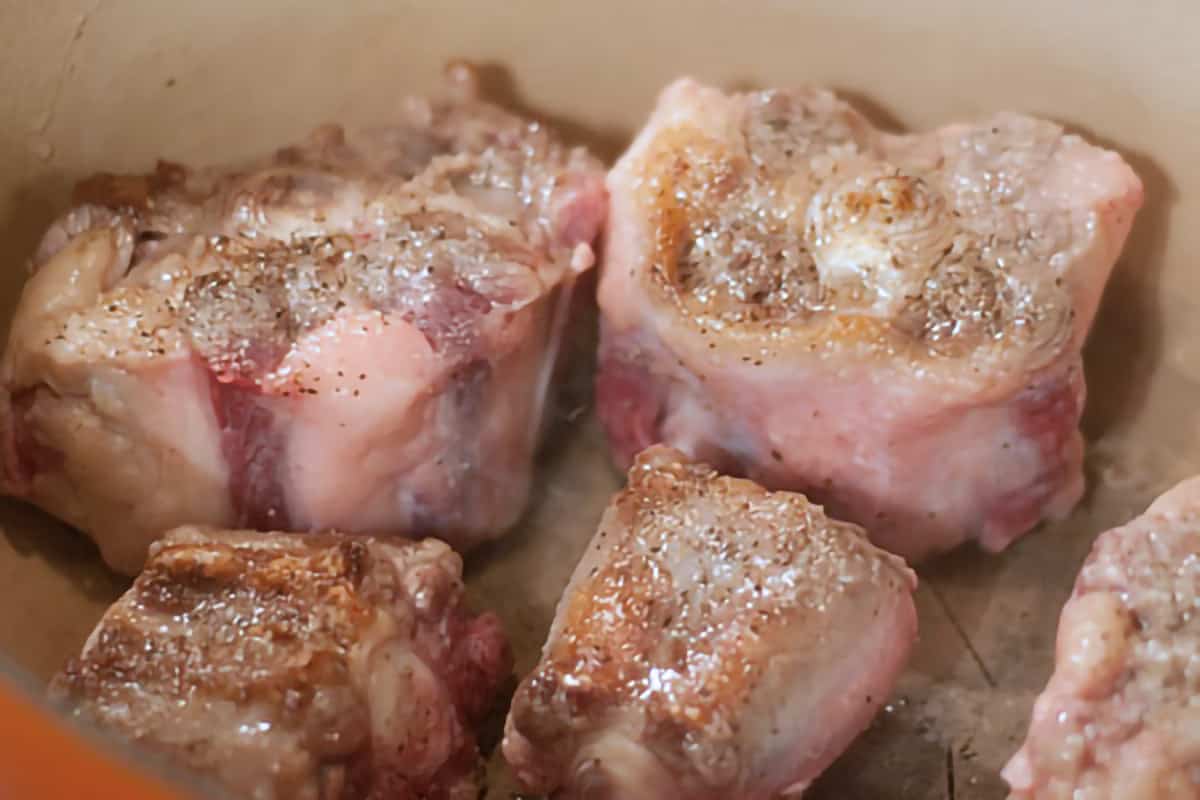 Oxtails being browned in a Dutch oven.